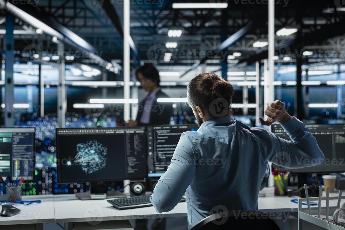 Data center engineer stretching at workstation to relieve back fatigue while using AI LLM assistant to perform maintenance. Server hub worker relaxing stiff back after long hours at computer photo