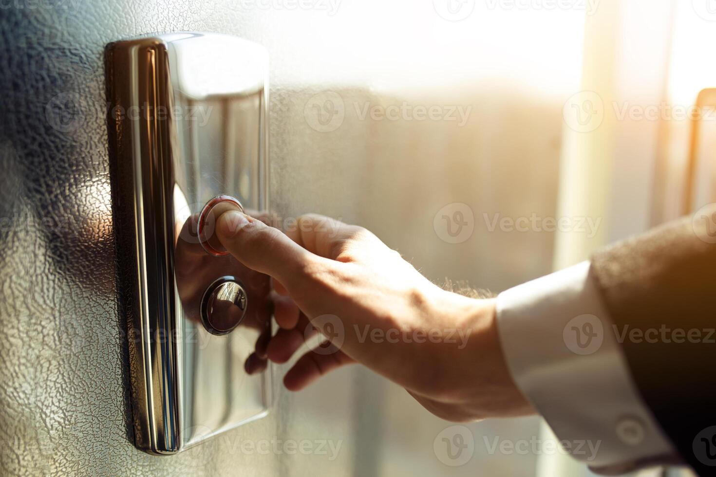 Man pushes the elevator button with his finger. Red button reflects the setting sun photo