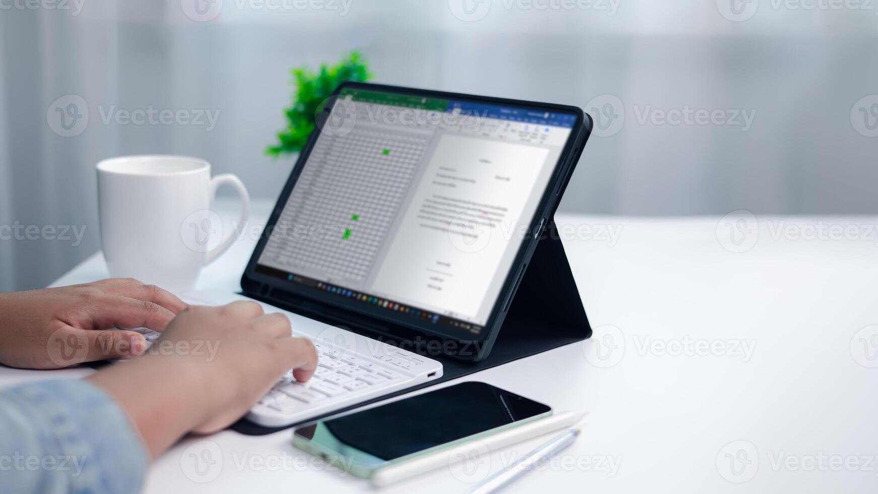 Close up of hands typing on wireless keyboard connected to tablet showing spreadsheet and document, concept of remote work, data analysis, project management, and business productivity. photo