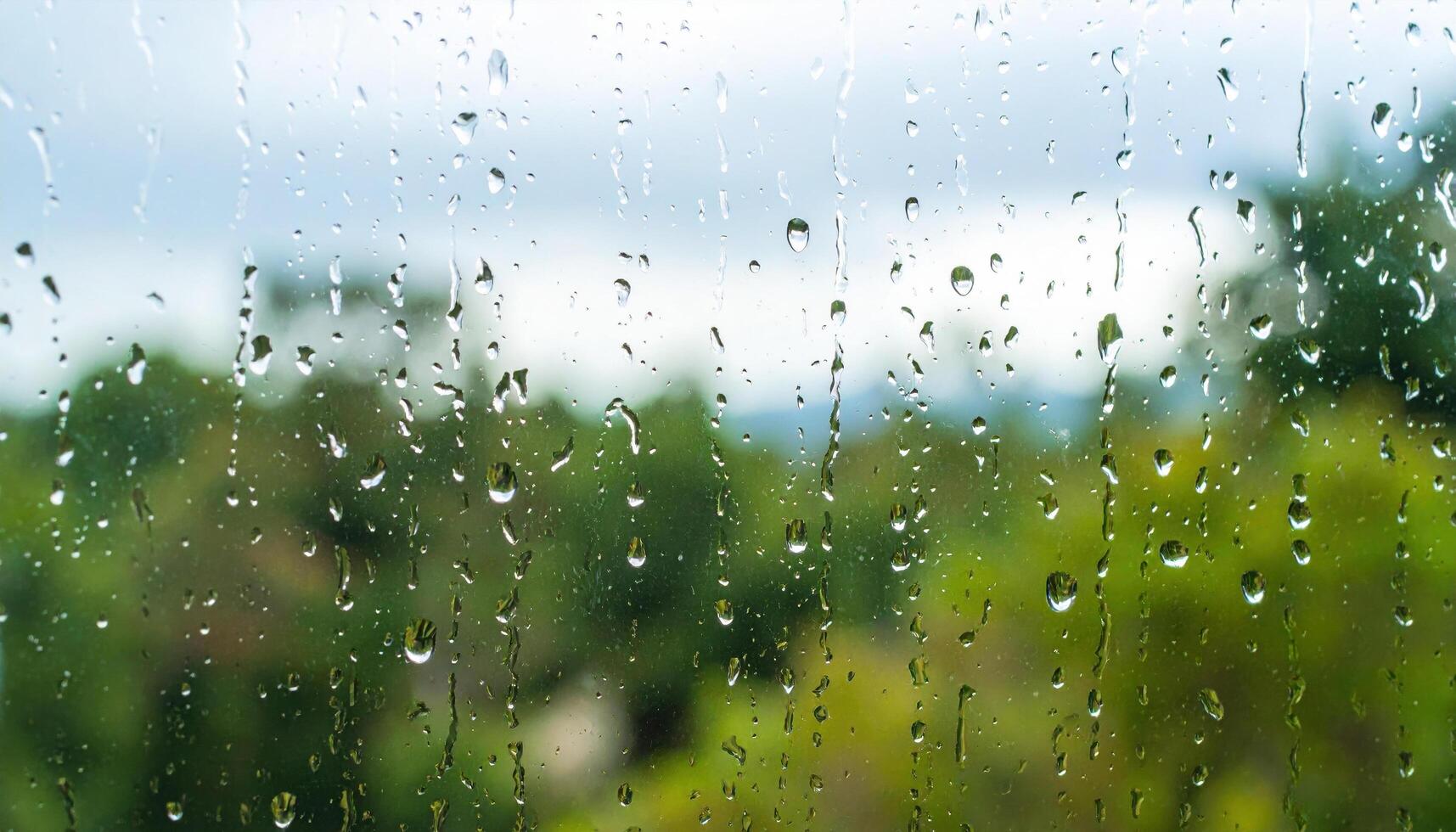 Raindrop on window glass with blurred green trees and cloudy sky background creating calm and peaceful rainy day atmosphere photo
