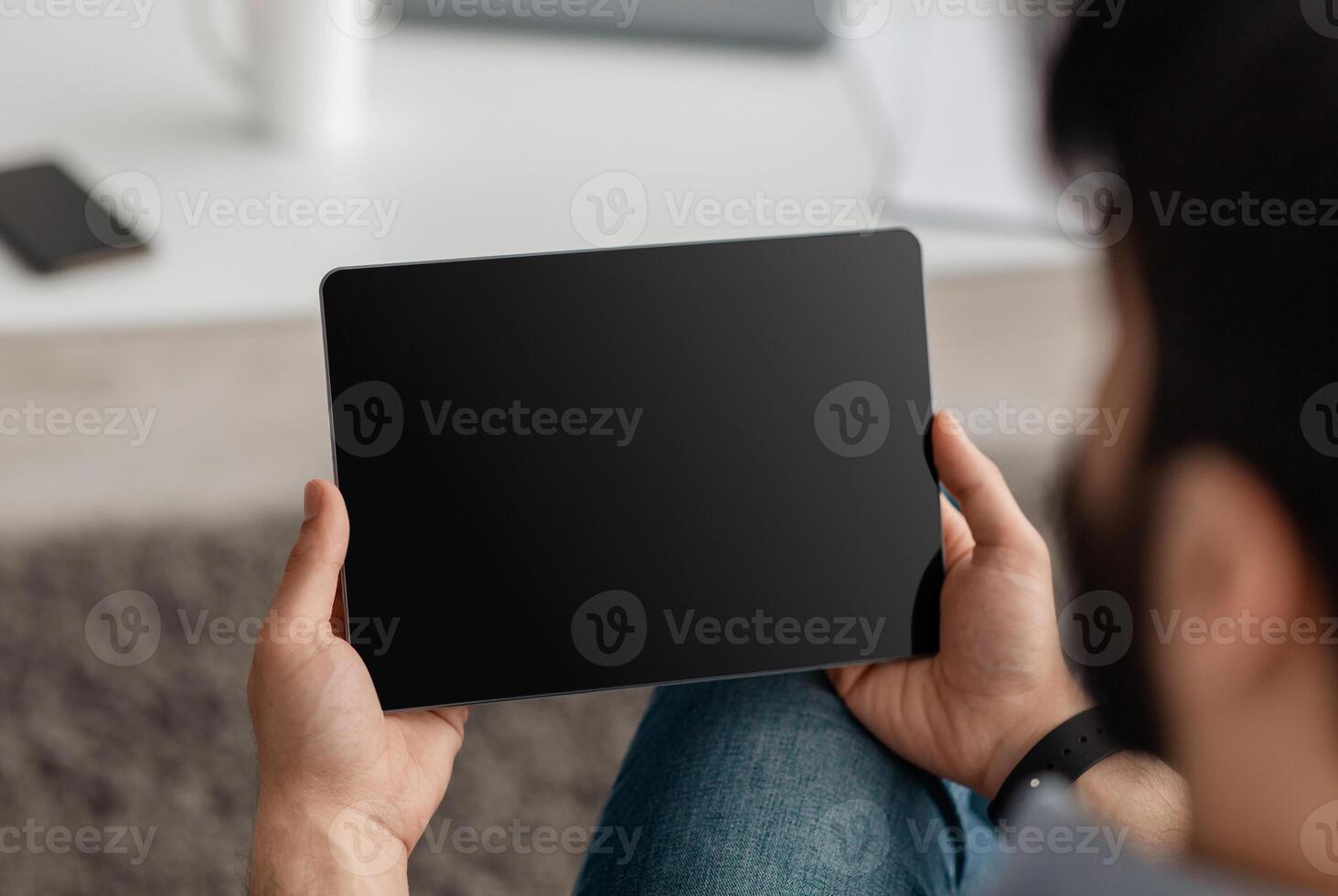 Unrecognizable guy using digital tablet with empty screen, browsing internet or showing new app, sitting on floor at home. Website advertisement concept. Rear view, mockup photo