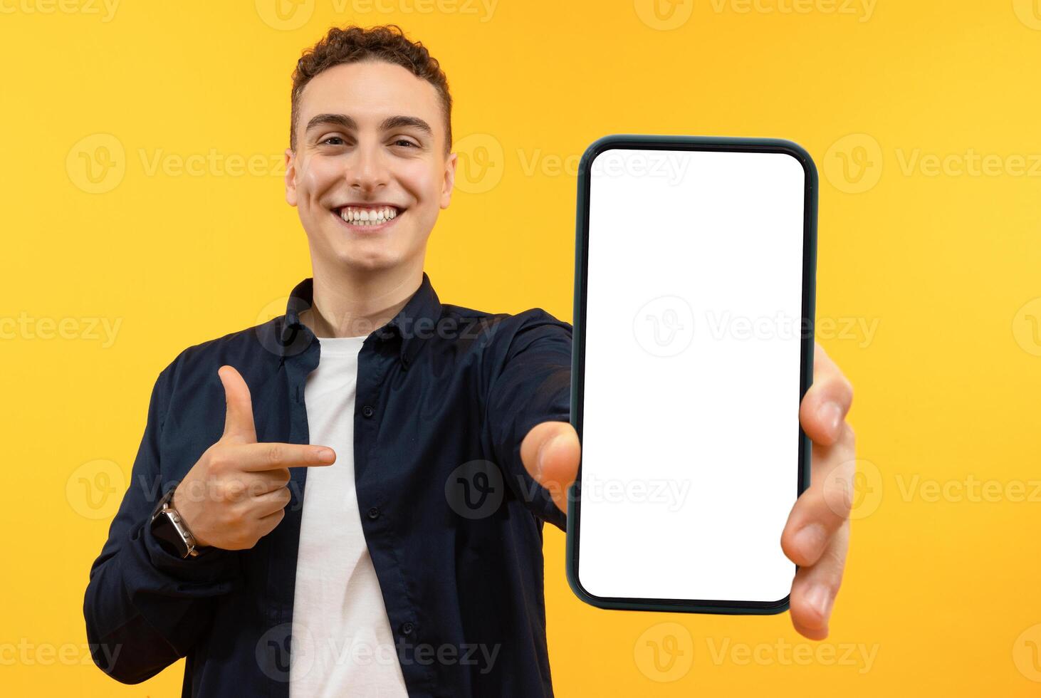 Recommendation. Portrait of excited guy holding big smartphone with white blank screen in hand, showing close to camera and pointing at device. Gadget with empty free space for mock up, banner photo