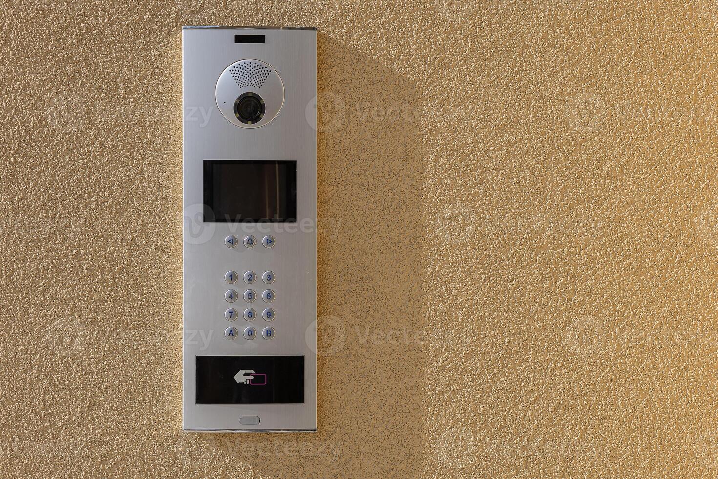 Modern intercom system with a built-in camera, keypad, and contactless access control panel mounted on a textured beige wall. Security, smart home technology and controlled building entry photo