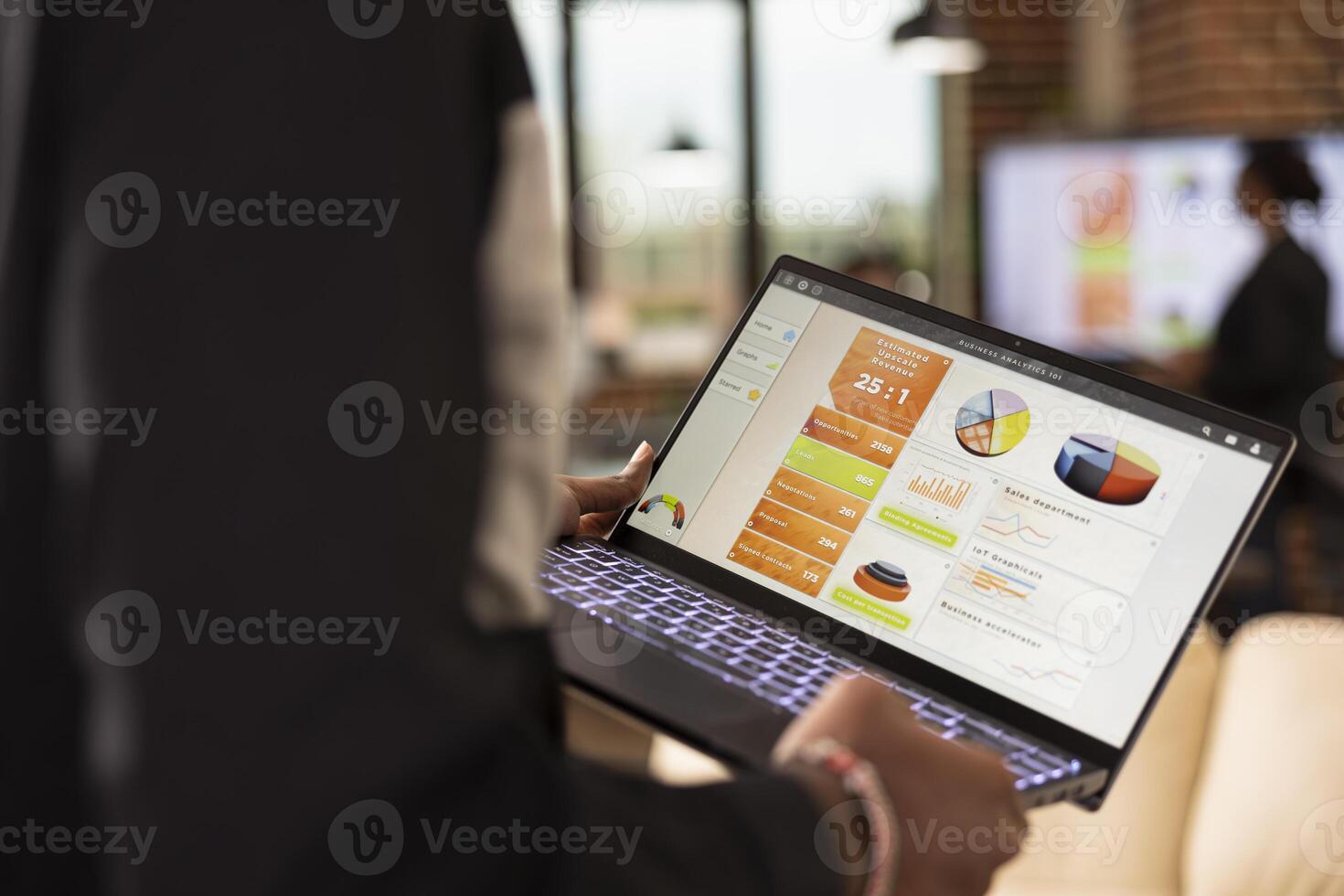 Selective focus on device screen displaying business analytics charts. Rearview closeup of african american person walking in office, reviewing financial graphs and evaluating kpi on laptop. photo