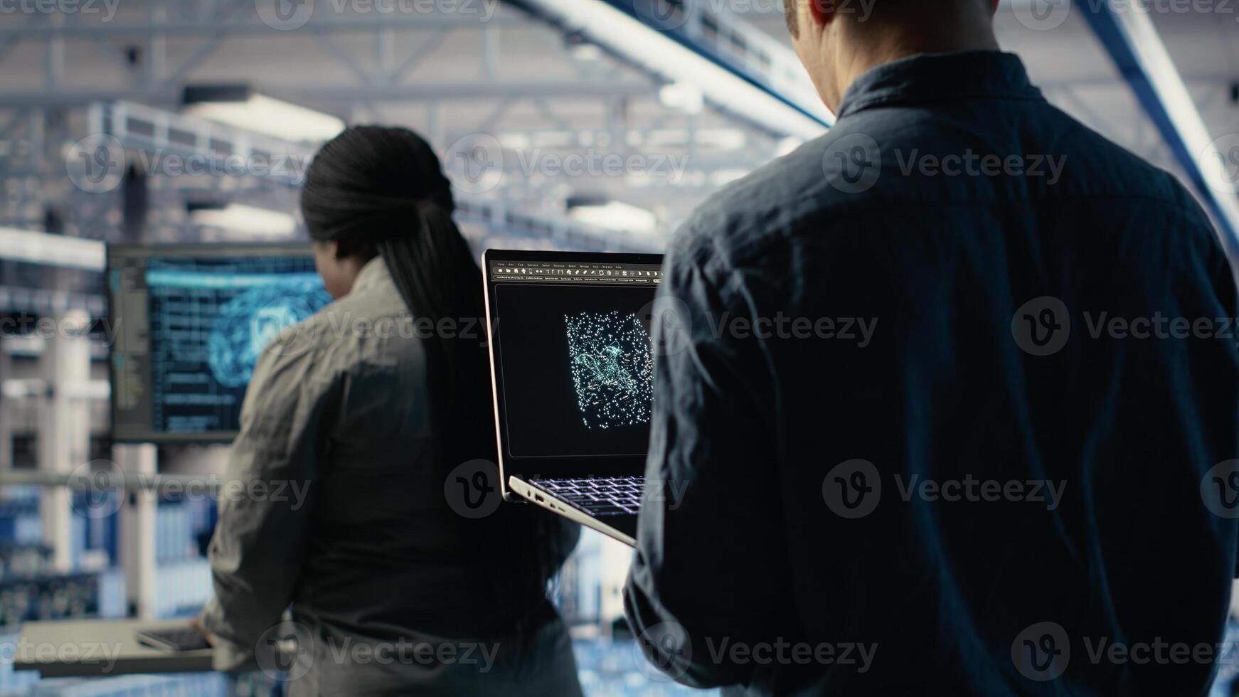 Software developer in data center checks AI dashboard using laptop during routine systems review. Server hub IT specialist tests artificial intelligence on notebook to check performance, camera B photo