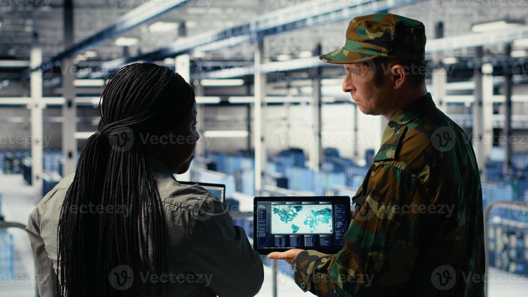 Military commander and female programmer in data center tracking coordinates using notebook software. Soldier and african american woman in server hub analyzing reconnaissance data, camera B photo