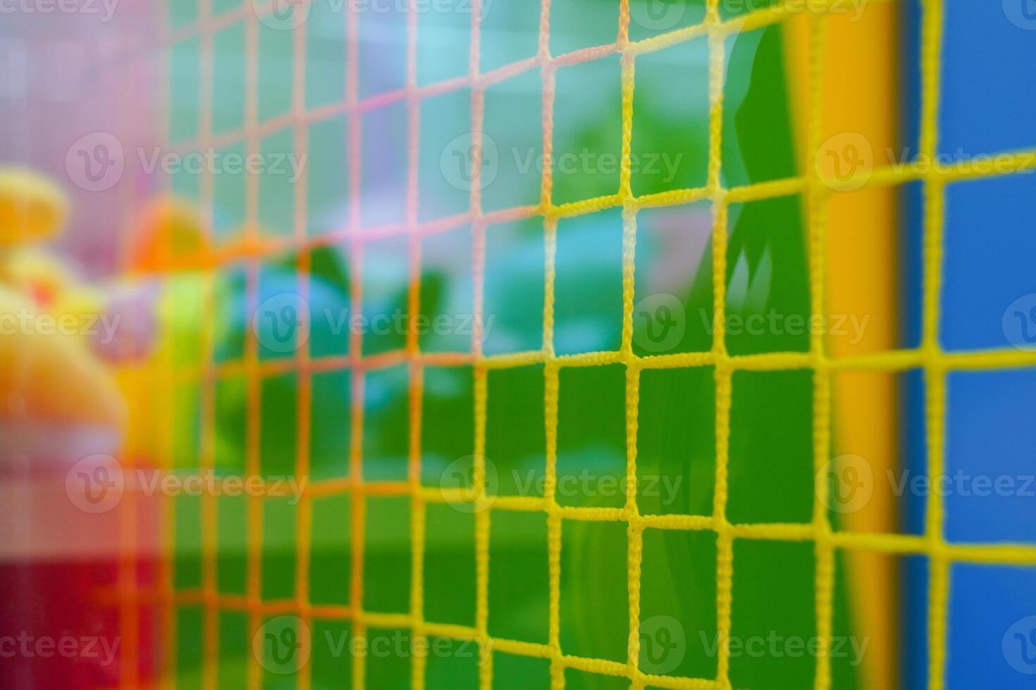 A vibrant mesh grid with yellow lines intersects colorful backgrounds of green and blue. Soft toys are visible through the grid, creating a playful ambiance. photo