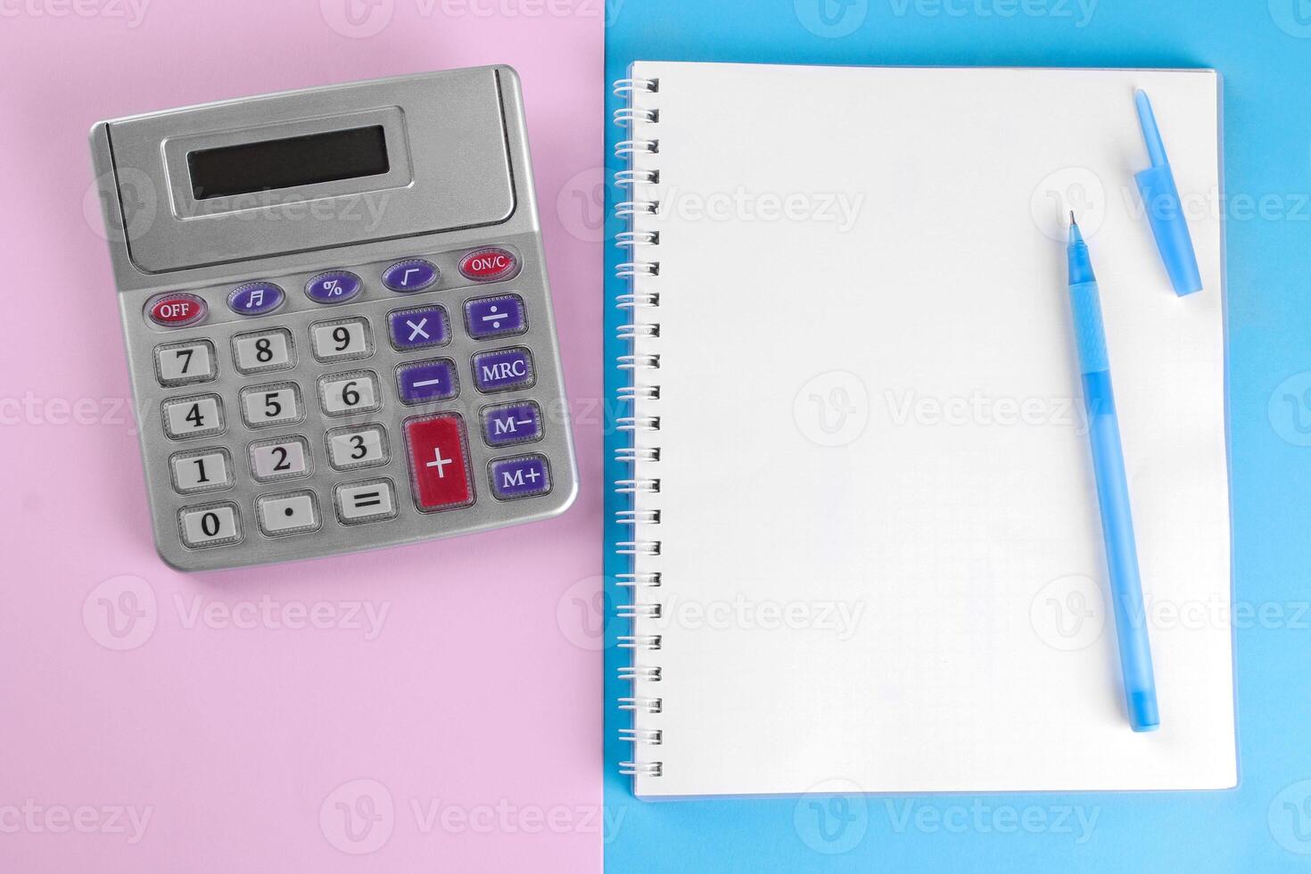 Calculator and notebook with pen on a blue and pink background. view from above. stationery photo
