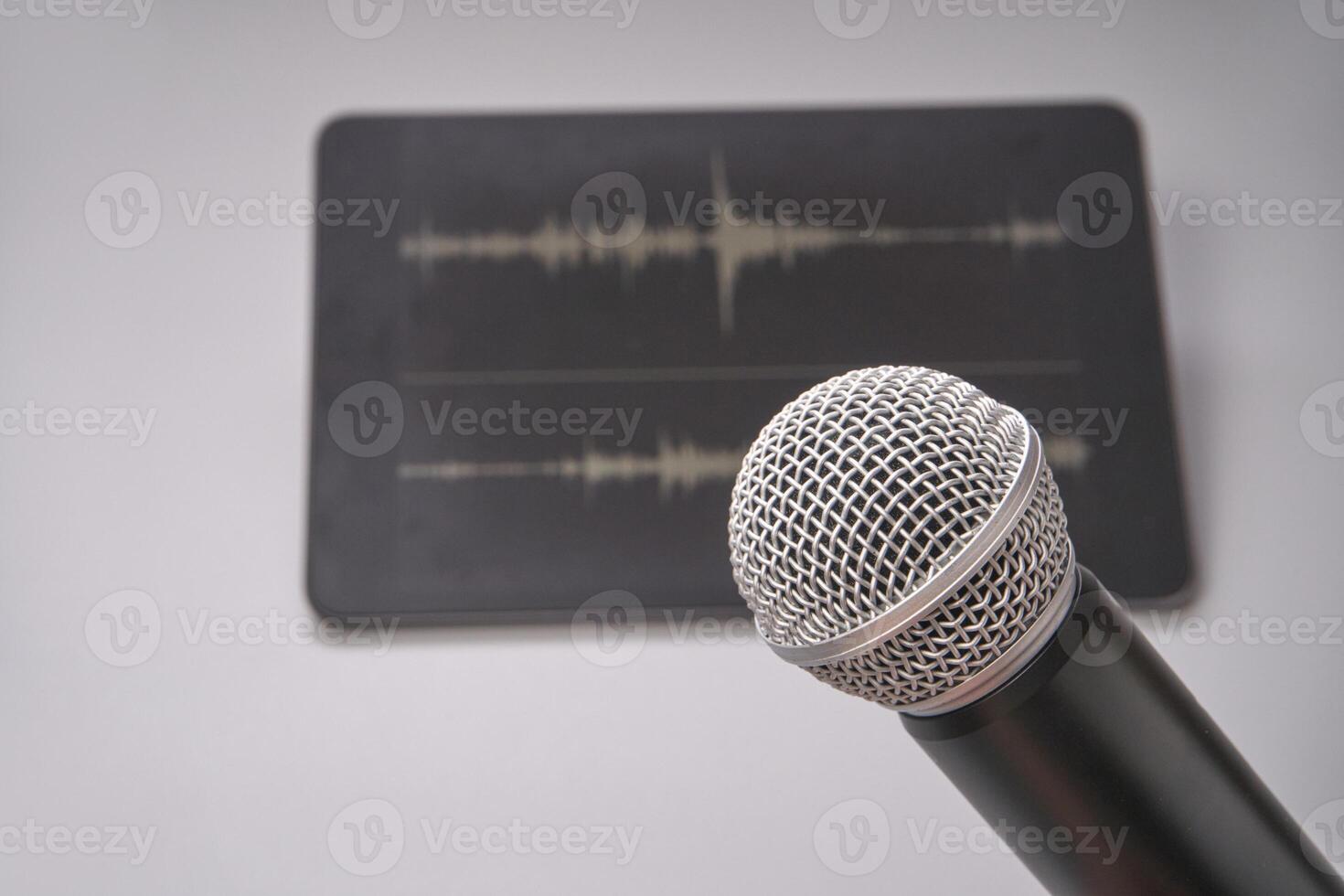 Close up of microphone in front of tablet displaying audio waveforms on a gray surface. photo