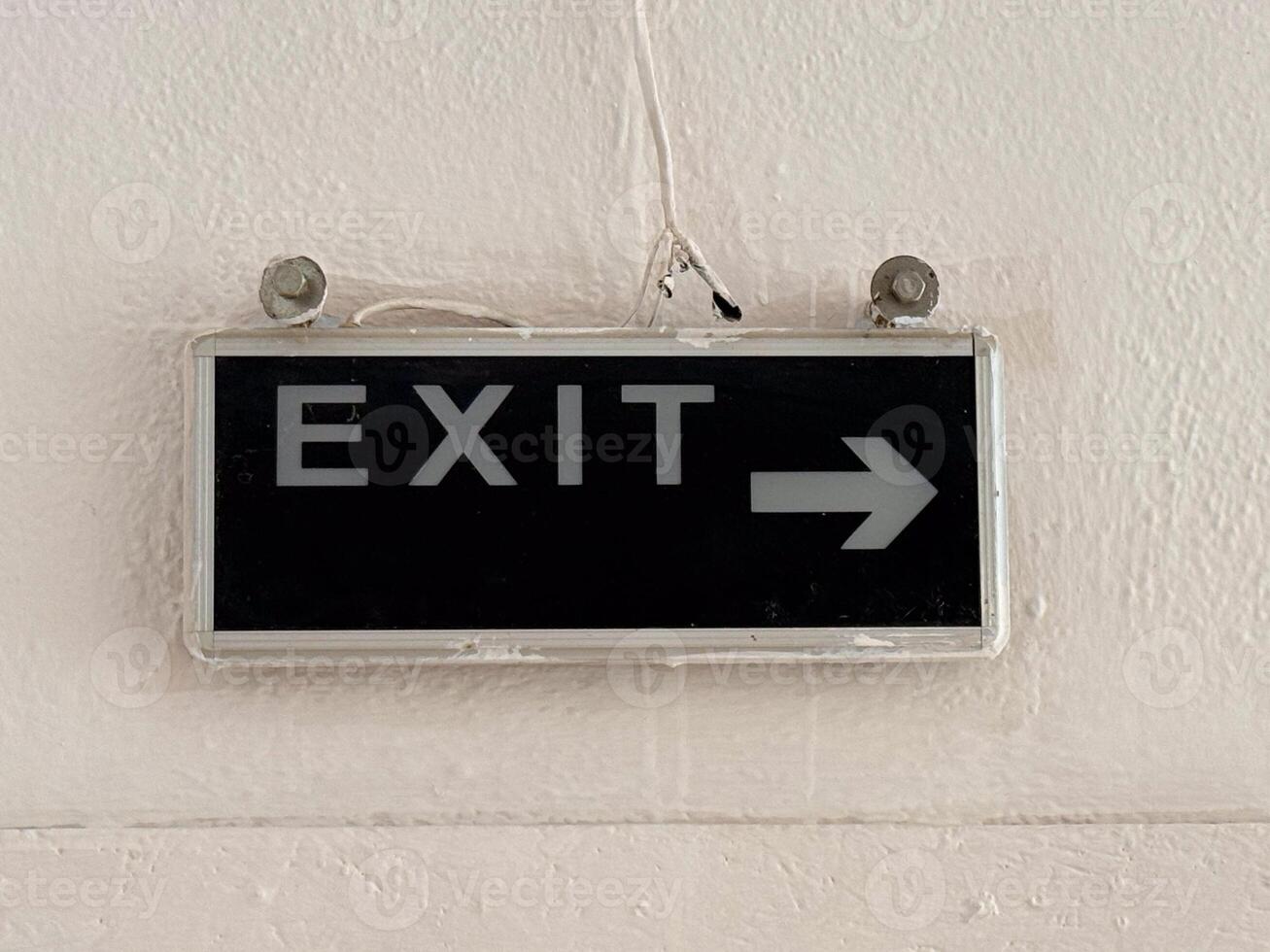 Exit sign with white letters and arrow on black background fixed to wall. Navigation, safety and communication represented through signage, typography and building orientation. photo