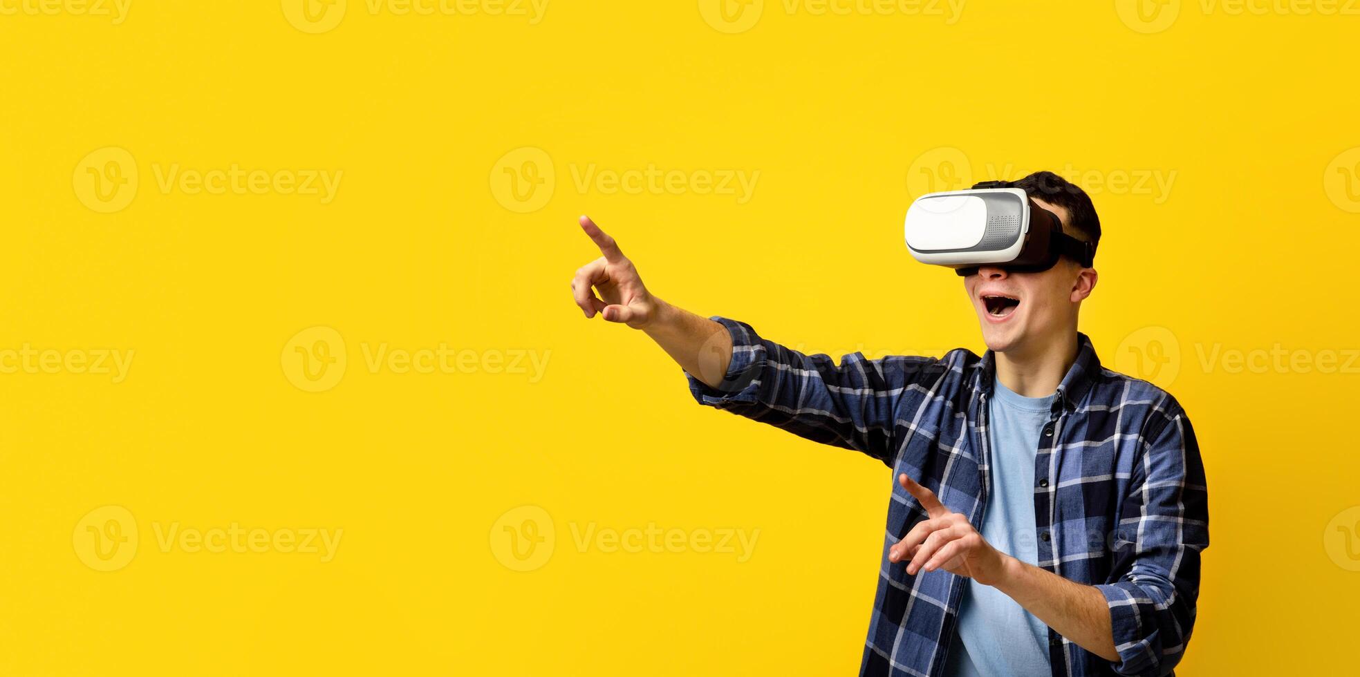 Cool young guy in virtual reality headset controlling cyber environment, pushing invisible button on virtual screen, orange background, banner design with copy space. Technologies and innovations photo