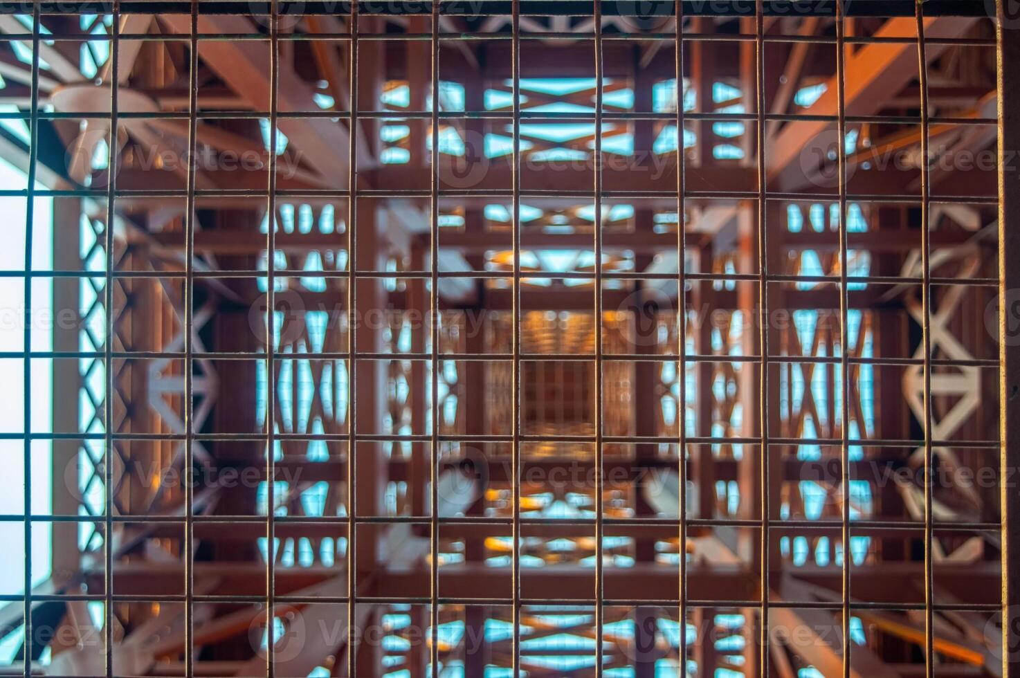 Abstract view of a tower structure through a metal grid, featuring geometric patterns and a sense of depth. The symmetrical design creates a visually intriguing composition. photo