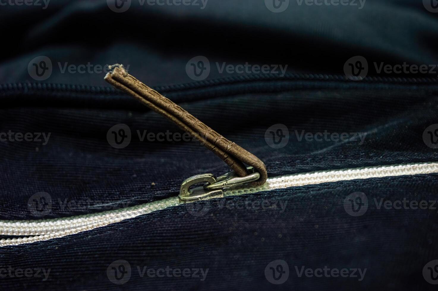 Close up on a black fabric with a zipper, featuring a brown leather pull tab. The zipper adds functionality and style to the material, suitable for various design projects photo