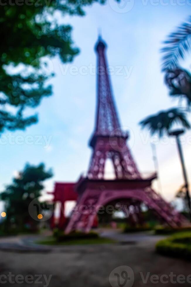 Blurred view of the eiffel tower replica in a park setting with trees and greenery. The tower is a prominent landmark, symbolizing travel and tourism in an outdoor environment. photo