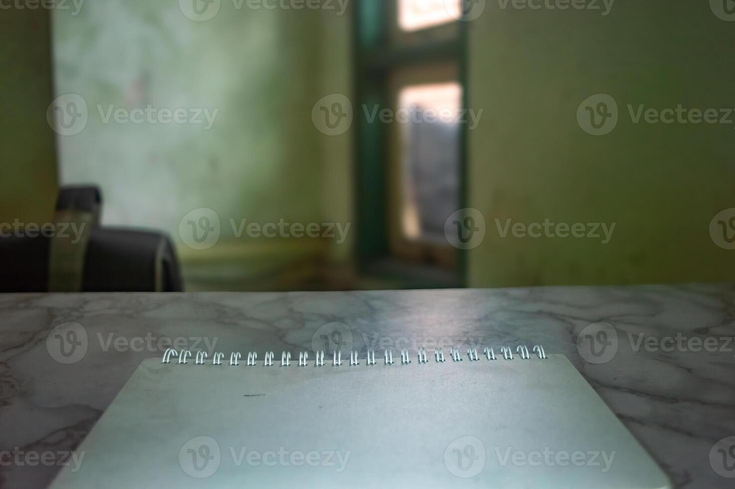 Blank notepad on a marble desk with a blurred room backdrop, ideal for mockups. The scene suggests a quiet workspace, perfect for showcasing designs or messages on the notepad photo