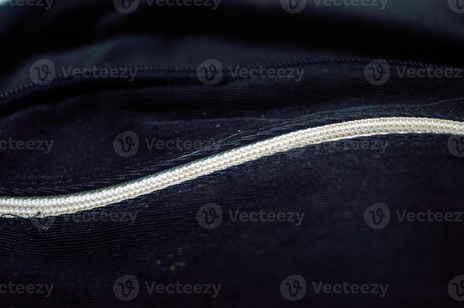 Close up on a black fabric surface featuring a white zipper. The image highlights the texture and detail of the materials, creating an abstract, minimalist composition photo