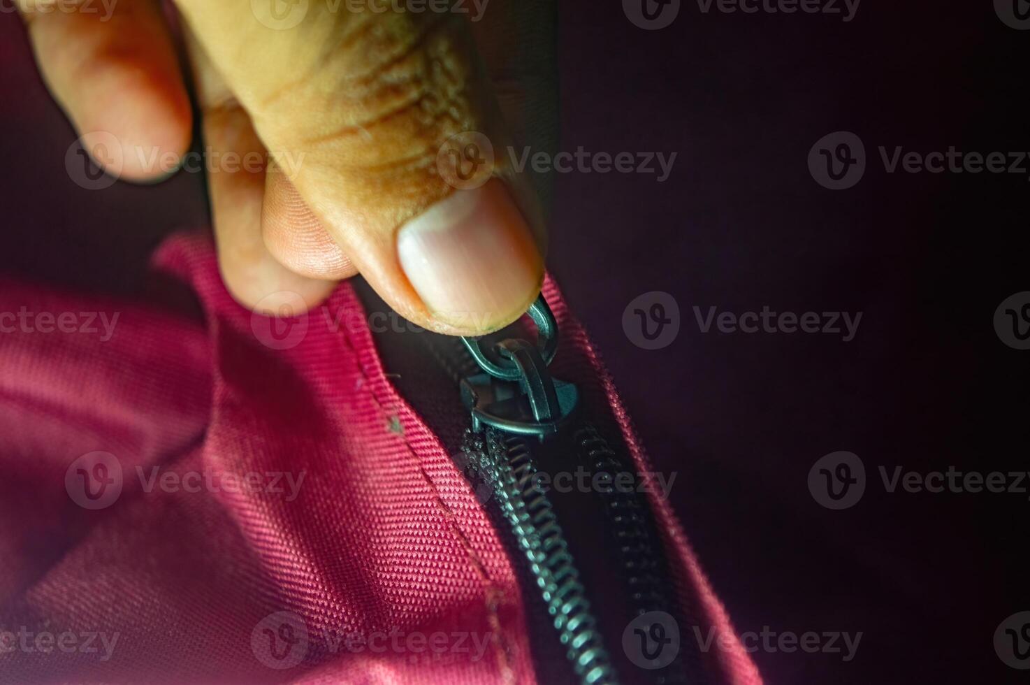 Close up on a hand zipping up a red fabric bag with a black zipper. The image captures the motion of securing the bag, emphasizing utility and convenience in a simple action photo