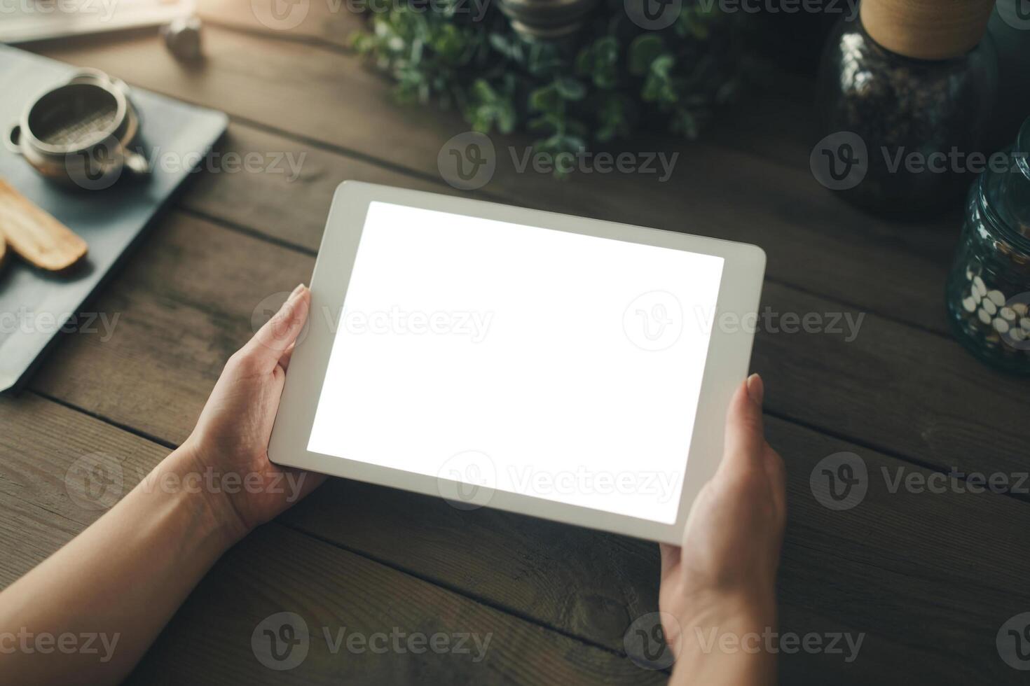Woman using tablet computer with blank screen at rustic wooden table in cozy home office setting, showcasing technology and remote work concept photo