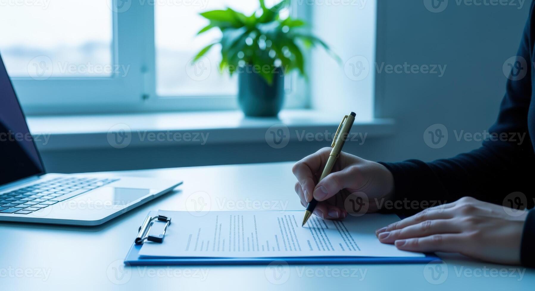 Signing Contract Document on Desk with Laptop and Window in Background, Focus on Hand photo