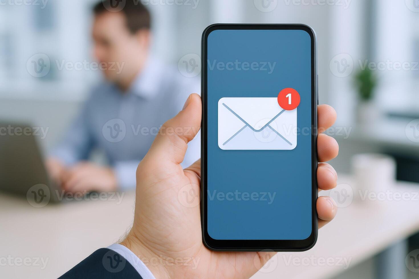 Close-up of person holding smartphone displaying email notification, office setting with blurred background photo