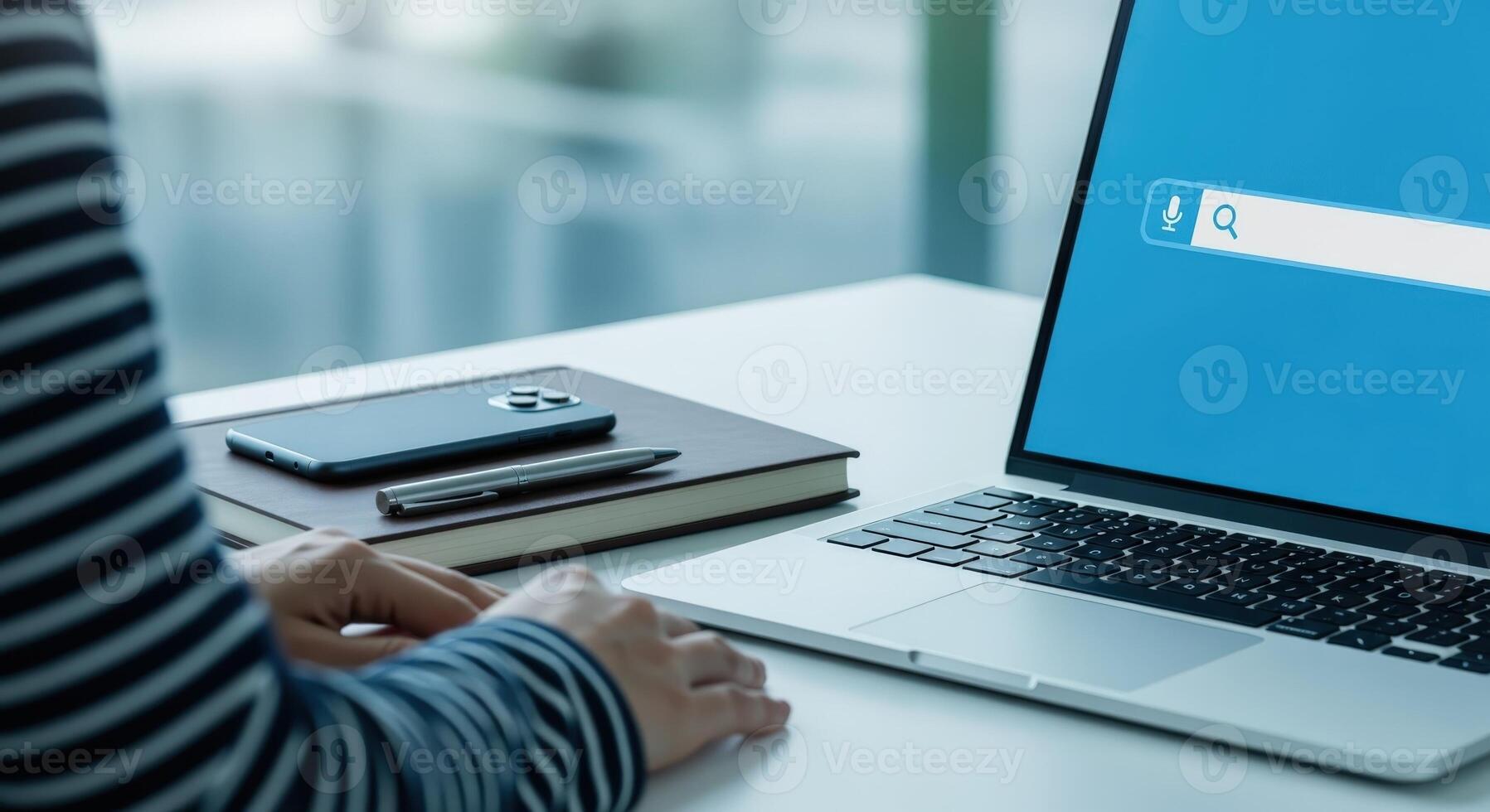Person Using Laptop with Search Bar Displayed, Desk Setting with Phone and Notebook photo