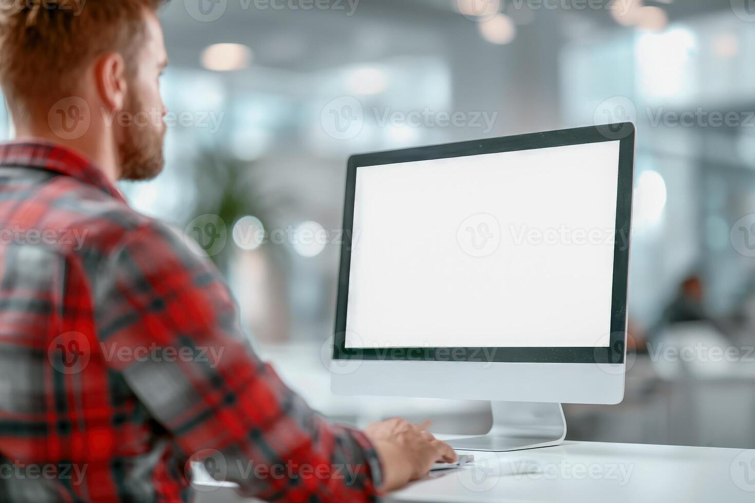Man working on a computer with blank screen in modern office environment, workspace mockup photo