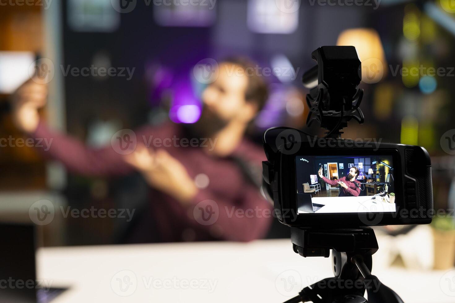 Focus on professional camera used by media star in blurry background hosting online show in neon lit studio, shooting vlog. Close up shot of high tech gear used by man during live stream broadcast photo
