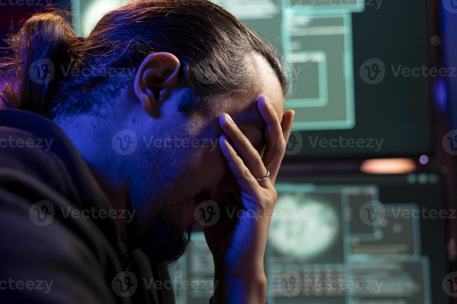 Closeup of sad hacker upset after failing to get malware past antivirus protection. Dejected cybercriminal in underground lair doing face palm, unable to develop data mining script to breach firewalls photo