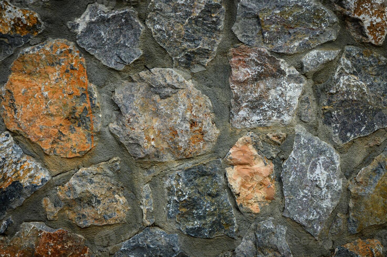 Close-up view of a natural stone wall texture, rustic background for design, construction or decoration use. Rough surface with authentic stone pattern. photo