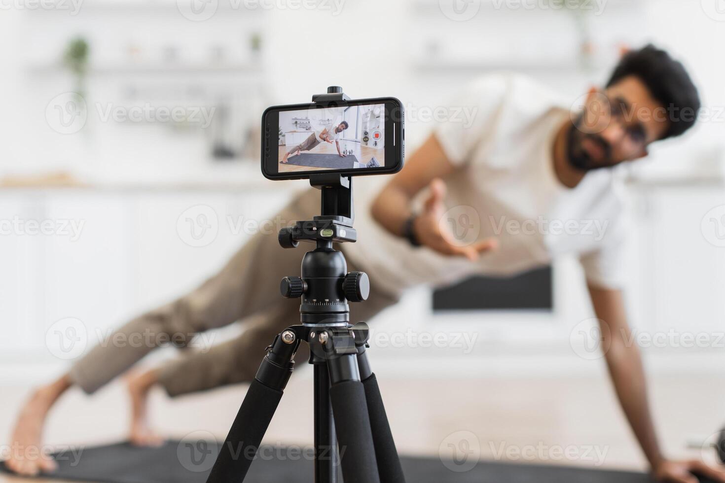 Middle-aged man performs plank exercise while recording fitness tutorial using smartphone camera setup. photo