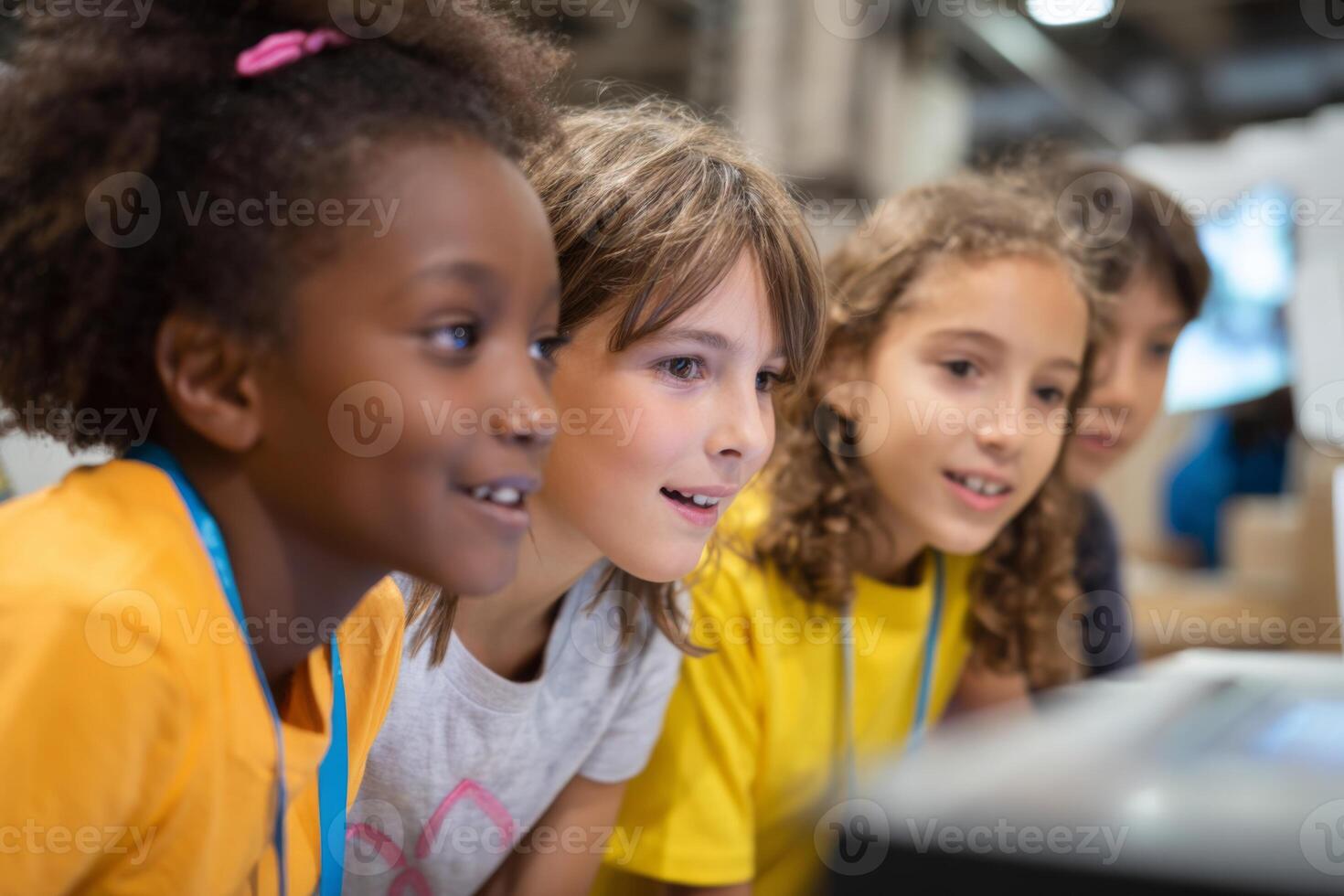Four children express joy and excitement while exploring technology together at a vibrant educational event. They focus intently on a digital display, surrounded by fellow participants photo