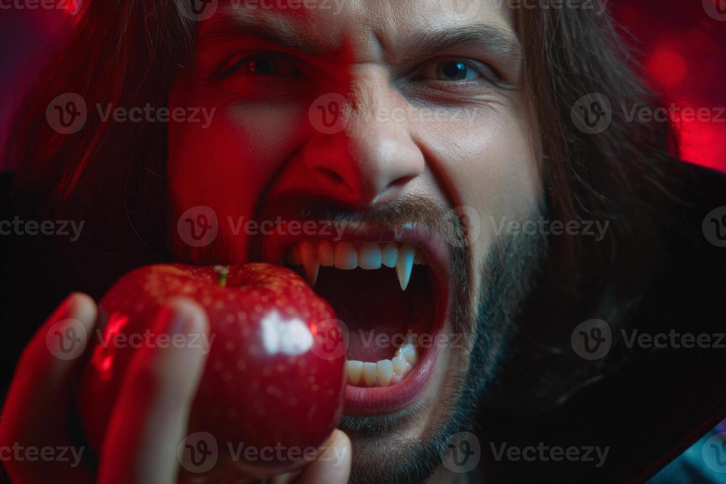 A young man displays fierce expression while holding a shiny red apple. His fangs suggest a playful vampire theme, enhanced by dramatic lighting creating an atmospheric effect photo