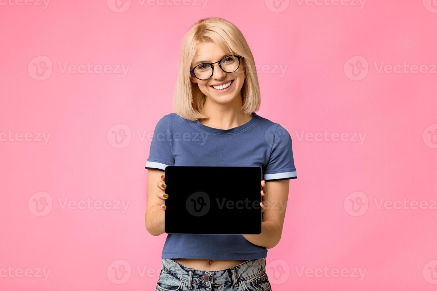 Cool application. Happy lady showing tablet computer with empty screen to camera, recommending new app. Woman posing over studio background. Digital tablet display mockup for advertisement photo