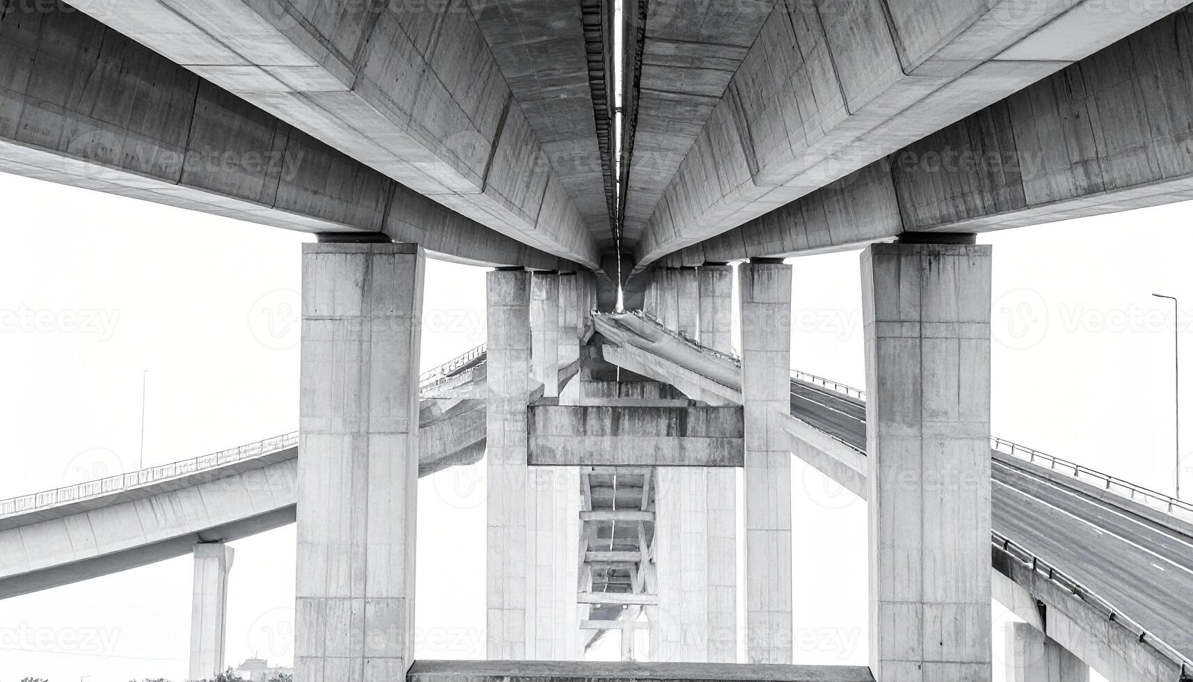 A grayscale view of a complex highway overpass structure. Pillars and concrete support beams form a network of roadways photo