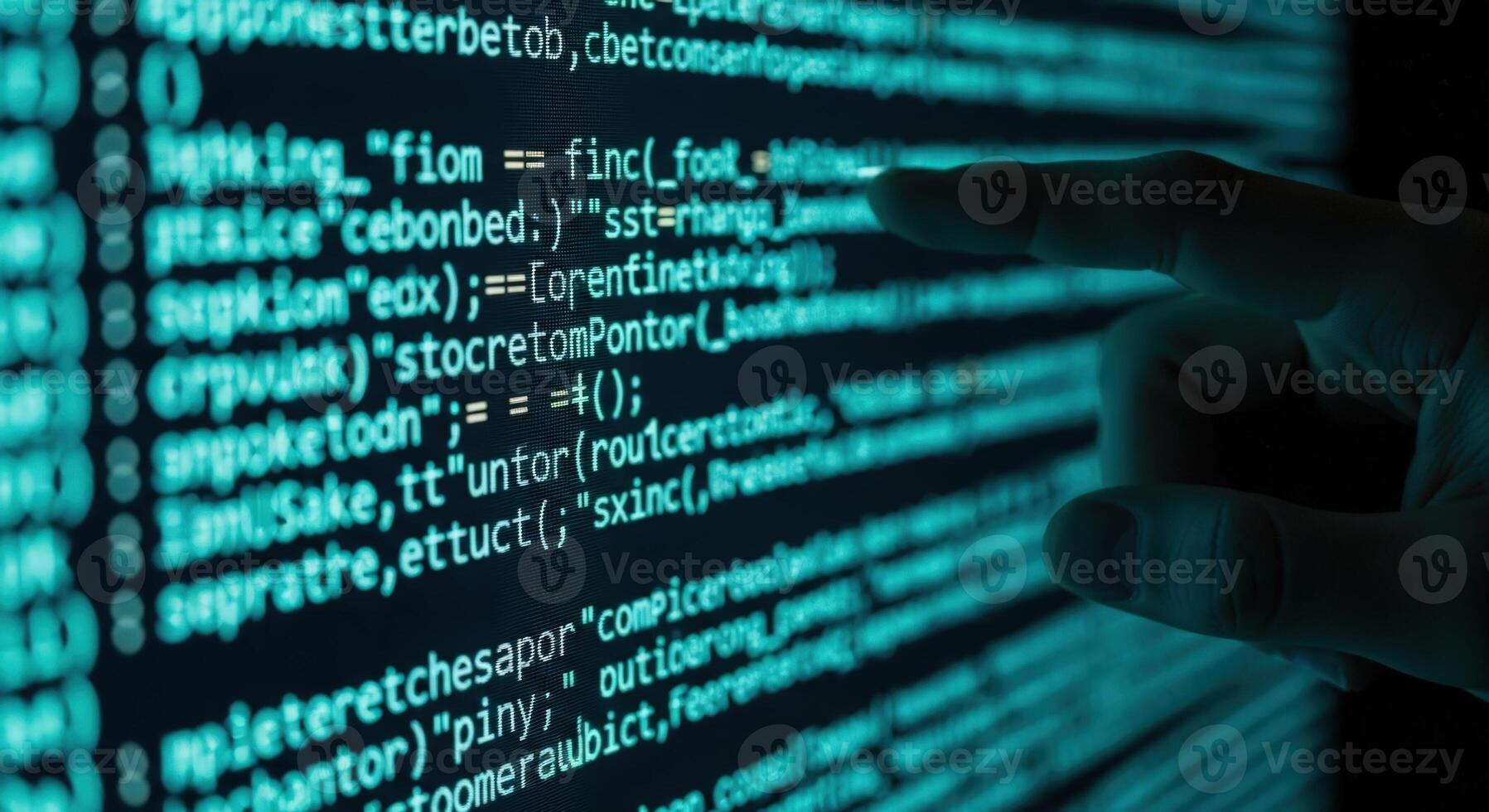 A hand pointing at lines of cyan code displayed on a computer screen in a dark environment photo