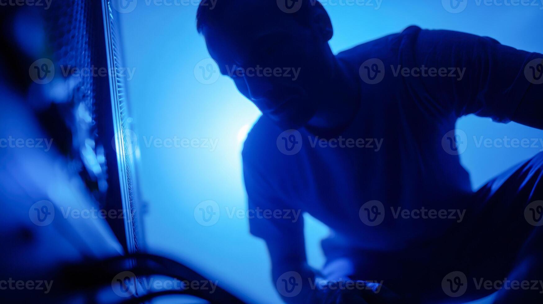 IT technician kneeling beside open computer while troubleshooting hardware issues in low light photo