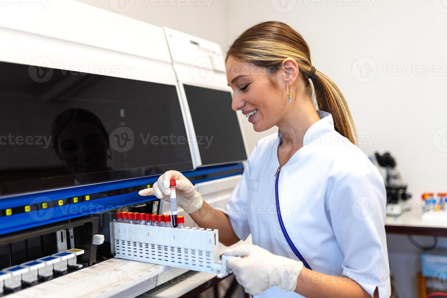 Lab tech loading samples into a chemistry analyzer female lab tech loading specimen for coagulation test analysis. photo