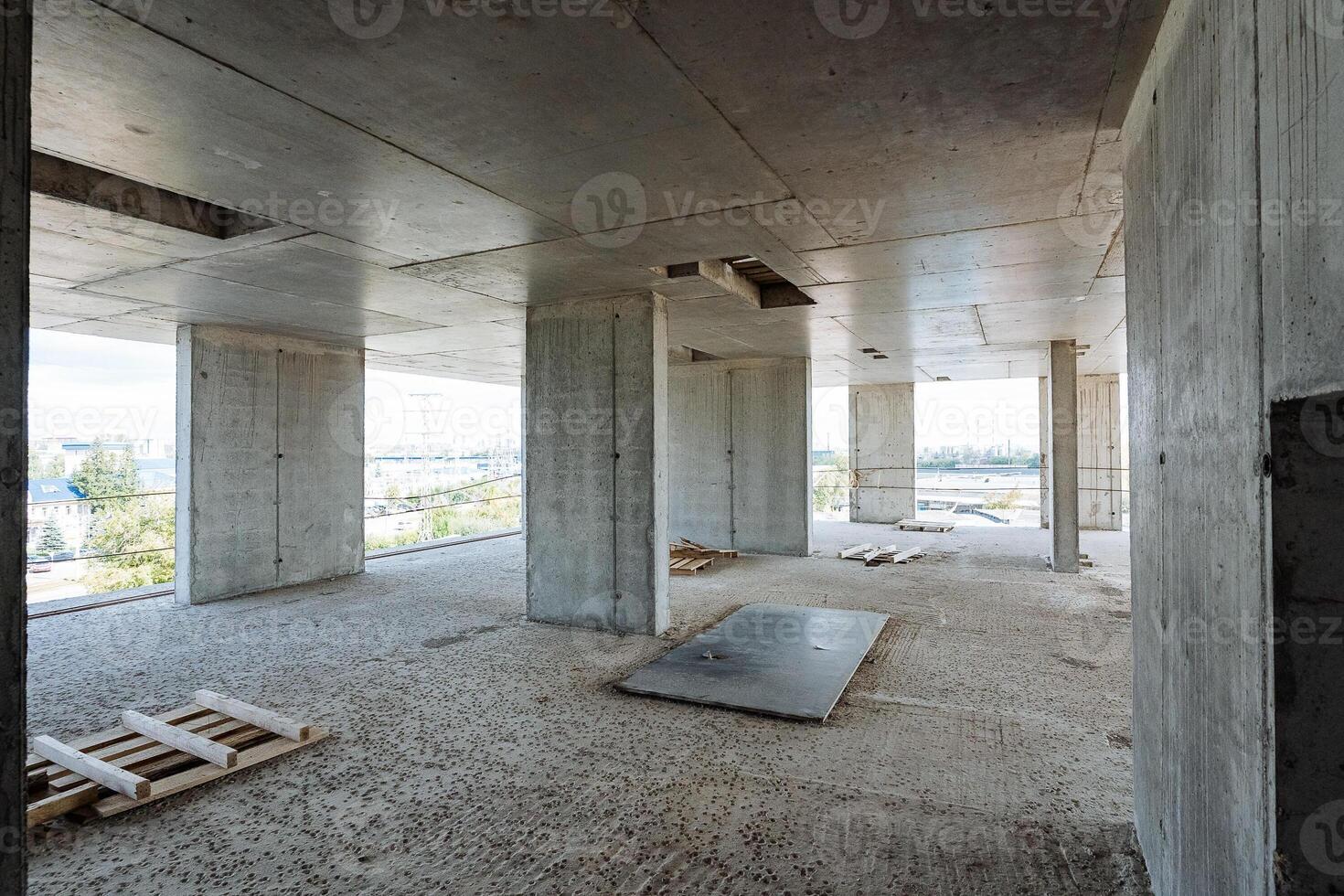 The room is significantly spacious and still devoid of any furnishings, situated within a structure that is currently being constructed, showcasing raw building elements and tools photo