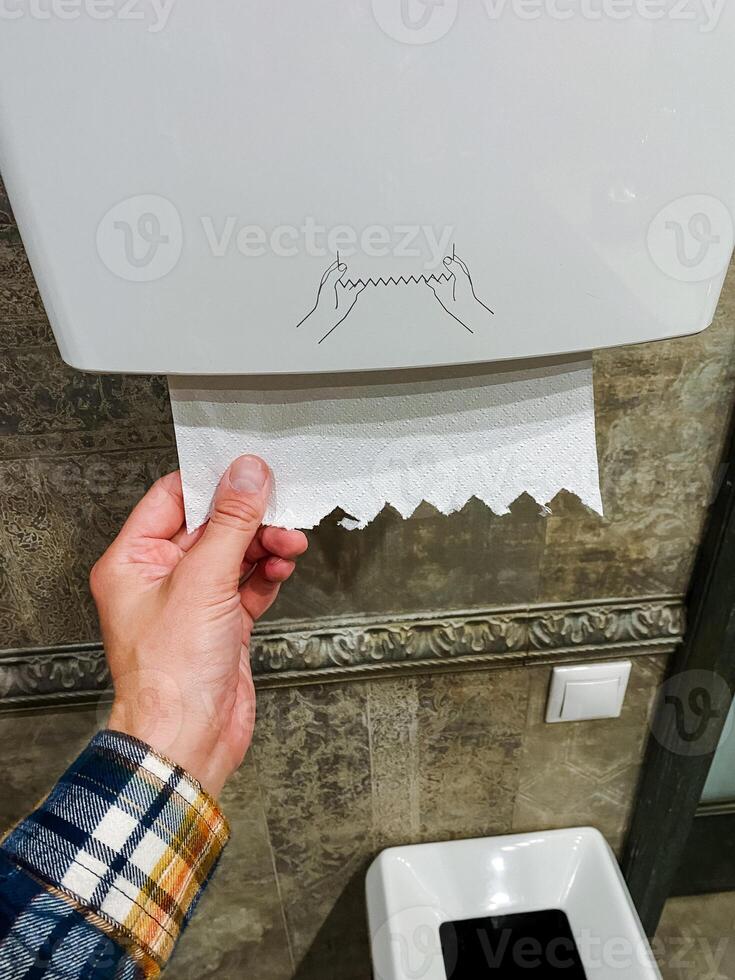 A person is methodically pulling a roll of multipurpose paper towels out of a specific paper towel dispenser designed for such products, which is often found in various establishments photo