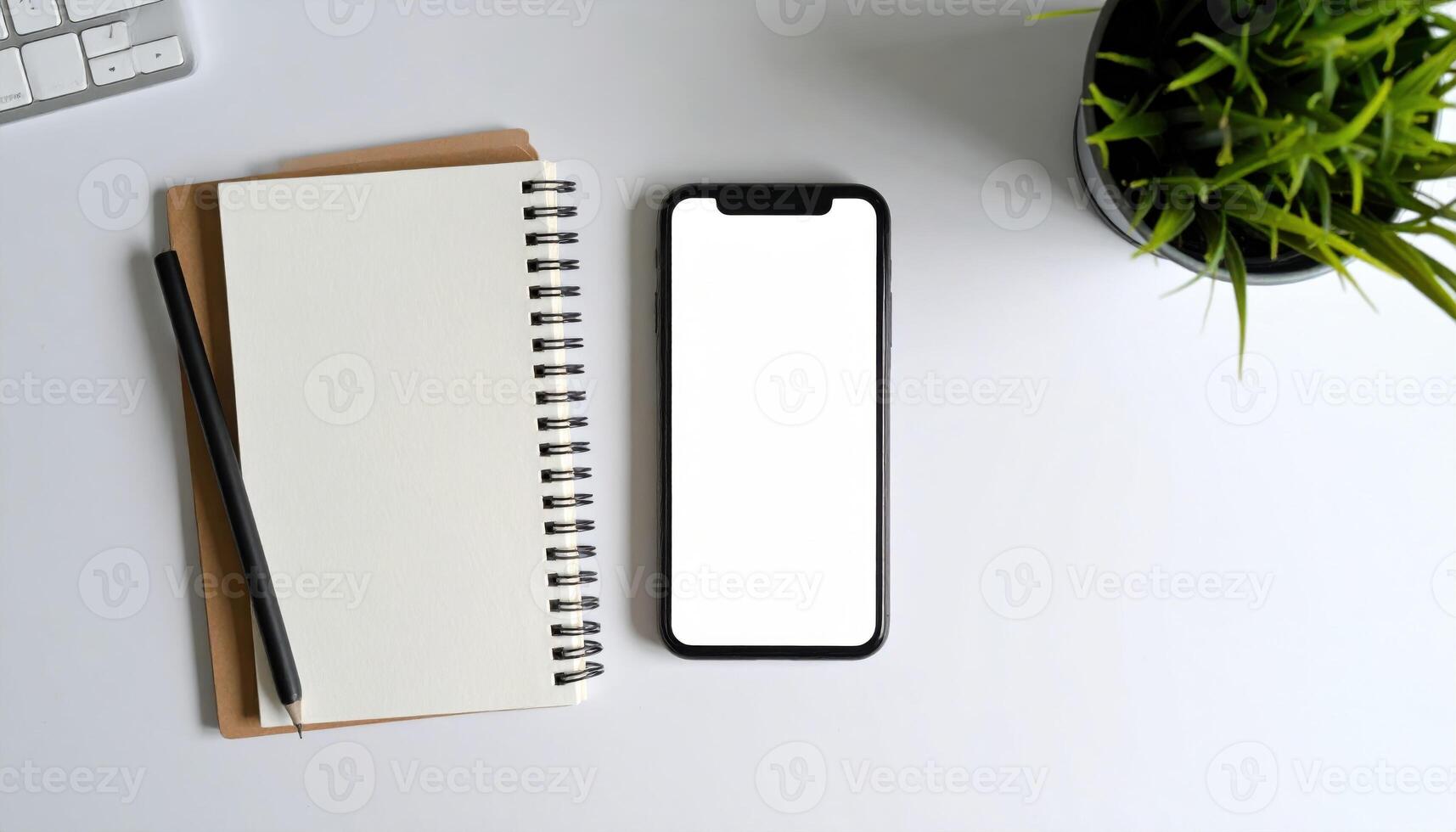 An open notebook with a blank page and a smartphone with a blank screen next to it, on a white desk with a pen and a plant. photo
