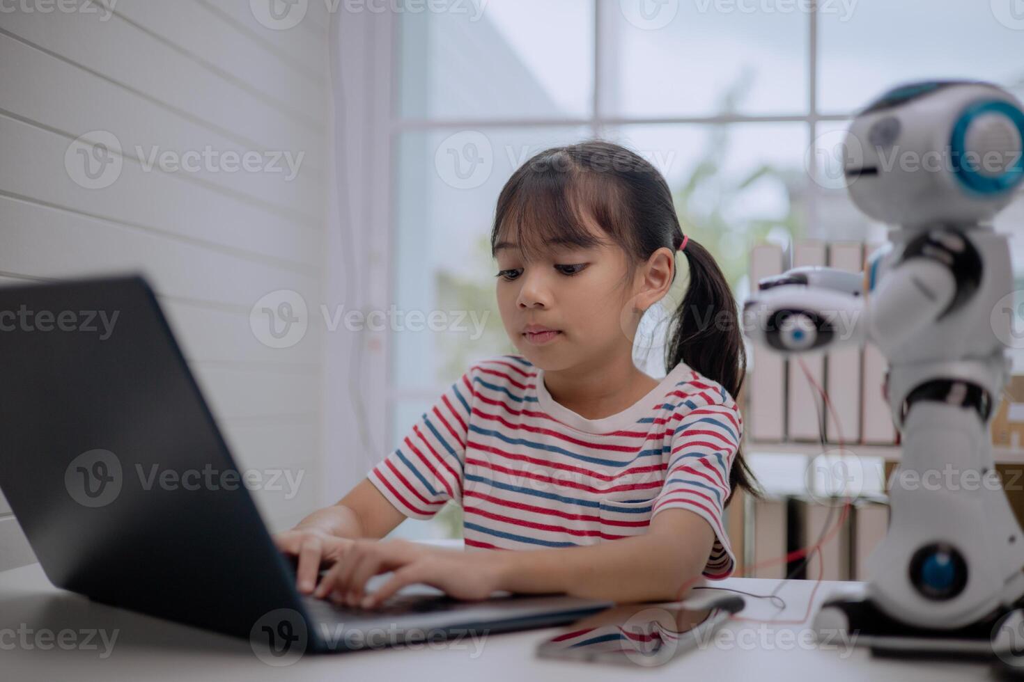 Asian girl typing on laptop with robot beside her, learning coding and robotics in STEM education. Concept of child programming, creativity, digital learning, innovation and future technology. photo