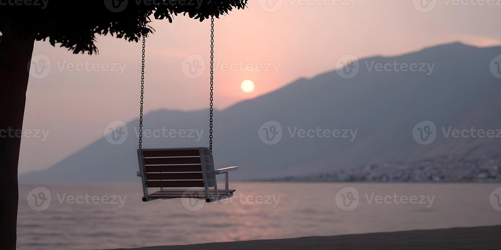 An empty swing hangs from a tree overlooking a calm ocean at sunset with mountains in the background photo