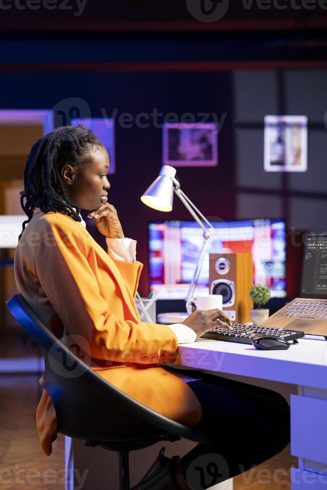 Software developer at desk using laptop, waiting for code to finish compiling, feeling bored. Impatient african american woman tired to wait for algorithms building scripts to finish photo