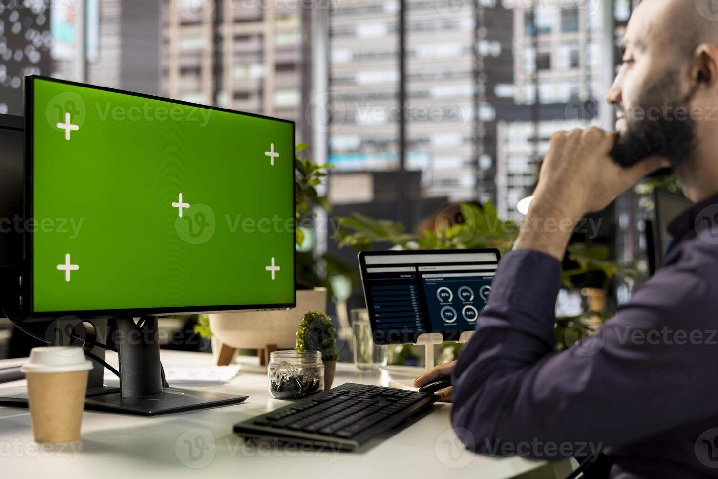 Middle eastern man working on accounting tasks next to green screen on pc, evaluating online analytics and performance metrics. Young employee reviewing data for a corporate briefing. photo