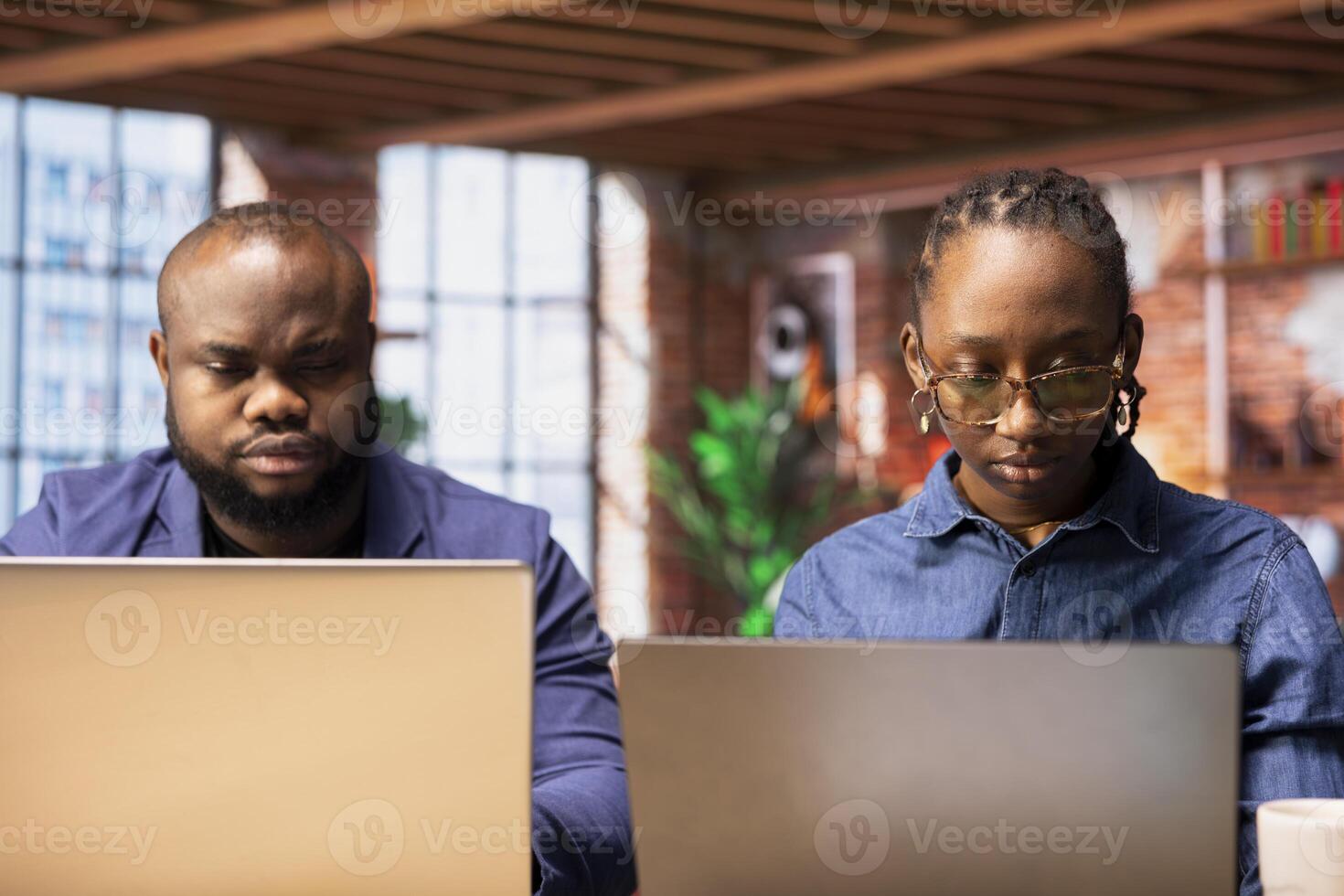 Black people both working from home at their designated office, using online digital tools on computers for tasks management. Completing operations efficiently from their comfortable house. photo