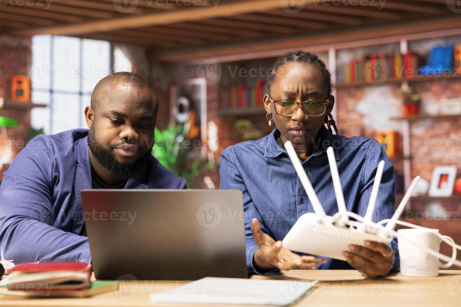 African american couple restarting their wireless router and checking network settings to resolve an internet error disrupting their freelance daily tasks. Signal loss during remote work. photo