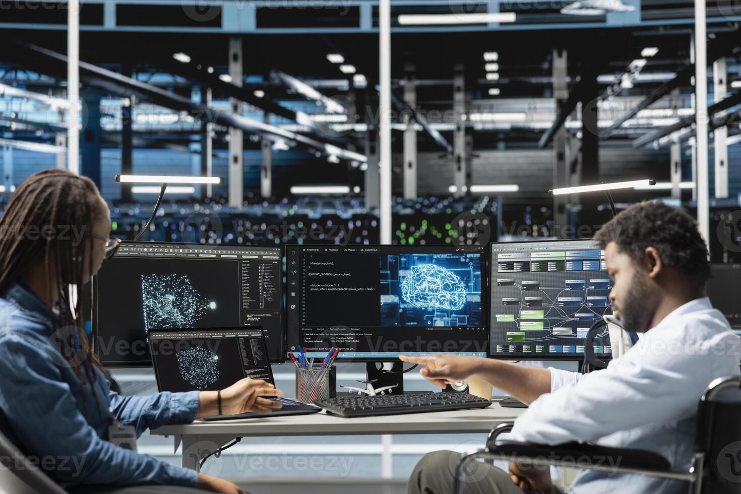 Data center engineer in wheelchair and coworker using AI visualization to oversee automated tasks. Worker with disability in inclusive server farm and colleague modifying systems based on analytics photo