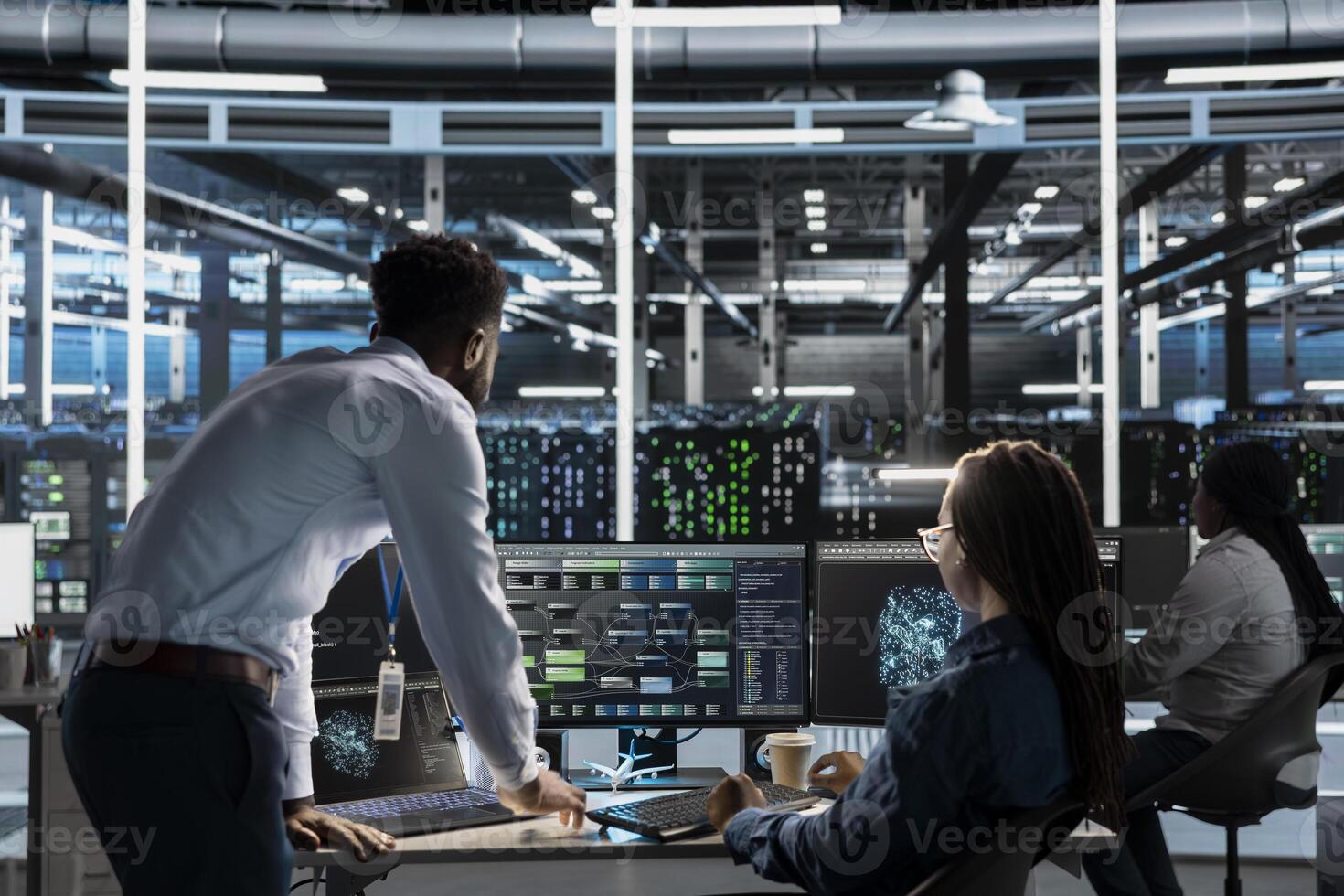 Data center manager supervises engineer using AI visual programming to optimize gear. Server farm team leader overseeing work done by worker colleagues using artificial intelligence analysis software photo