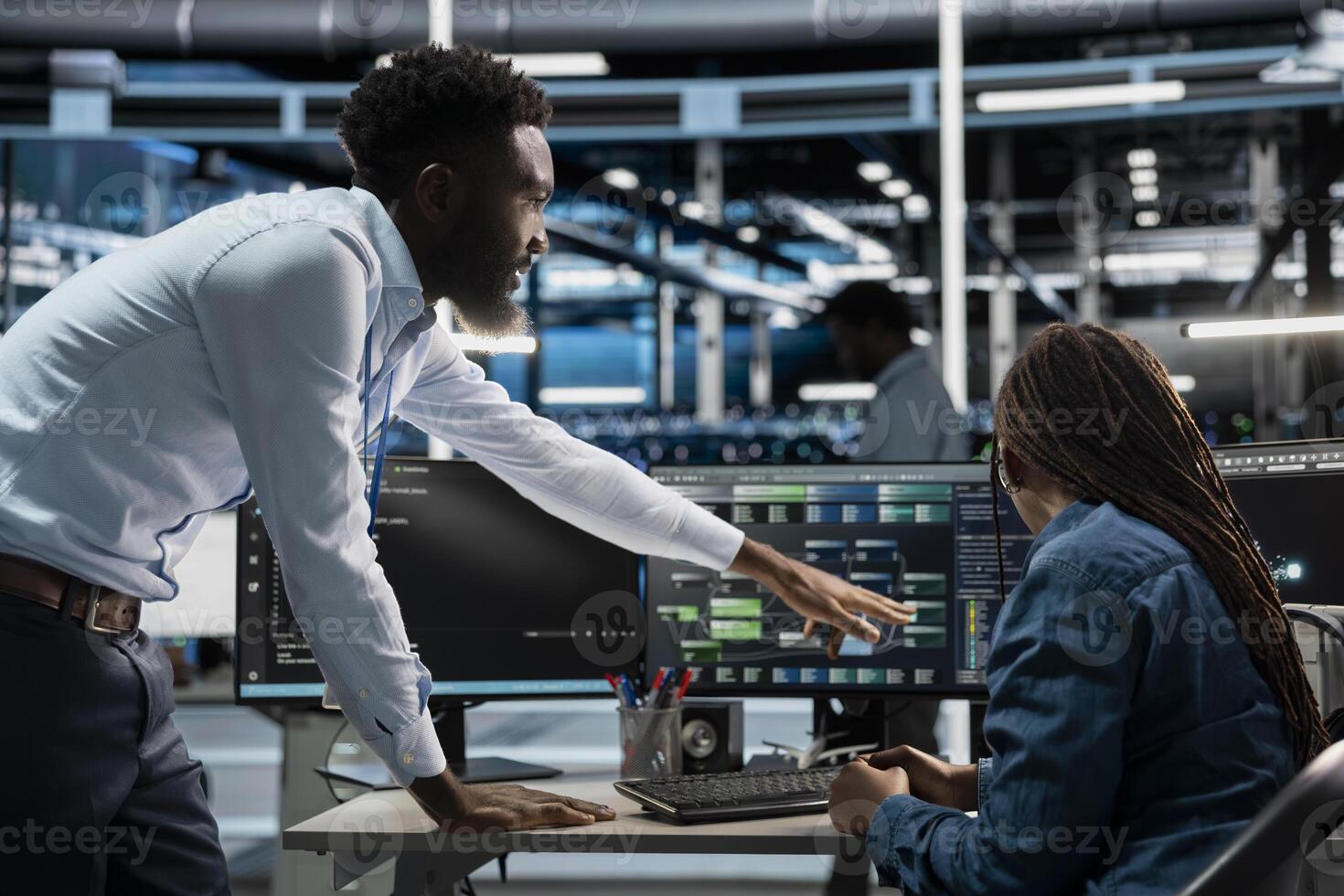 Data center supervisor offering feedback to engineer programming equipment used for machine learning training. Server farm manager and staff member upgrading artificial intelligence systems photo