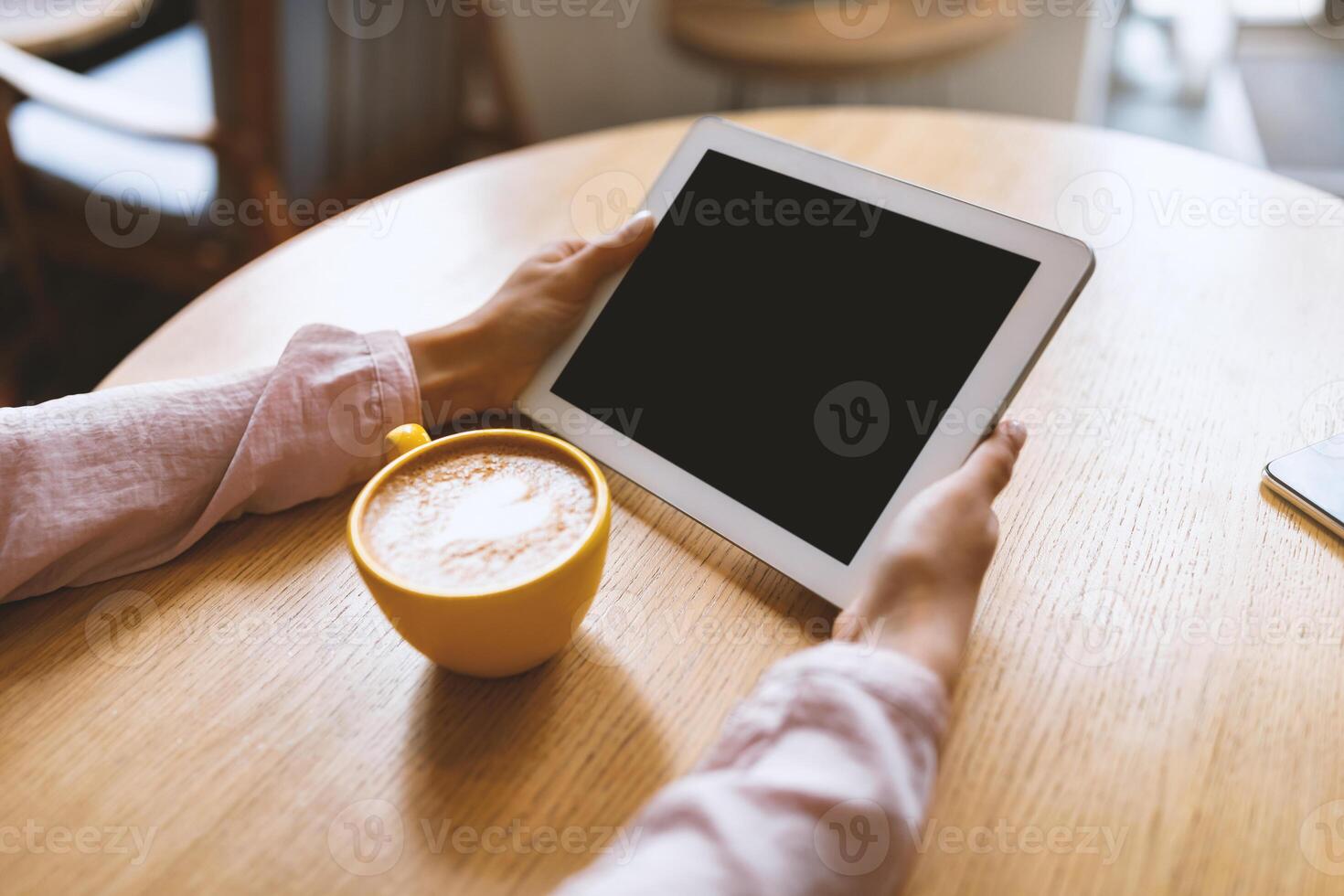 Unrecognizable lady using digital tablet with blank screen, having call while sitting at table in cafe and drinking coffee. Mockup for your design or website photo